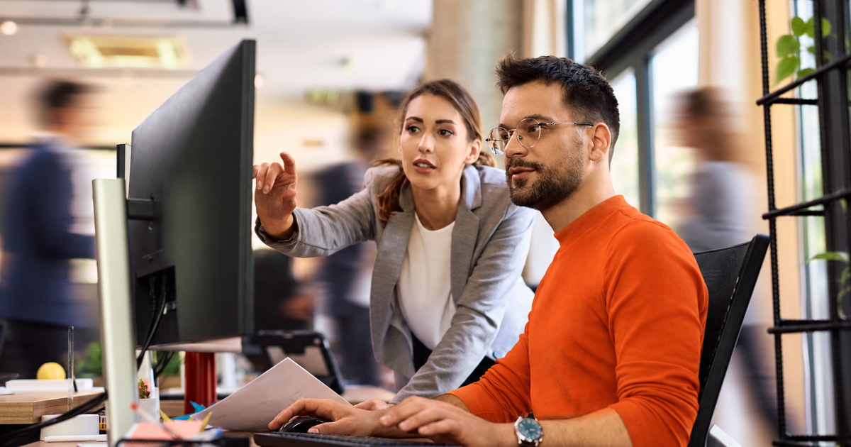Woman pointing at screen while sitting man types