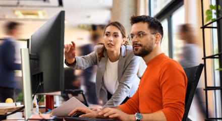 Woman pointing at screen while sitting man types